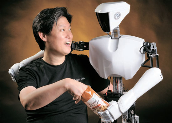 米バージニア工科大学のデニス・ホン教授が、今年のロボカップヒューマノイド（人間型ロボット）成人型部門で優勝した「チャーリ２」と肩を組みながらポップコーンを食べている。 「チャーリ２」は身長１４０センチのロボットで、 韓国作家オム・ユンソル氏が外観をデザインした （写真＝バージニア工科大学ロメーラ研究所）。