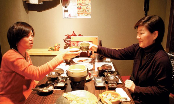 東京の韓国料理店で日本の女性がマッコリで乾杯している。