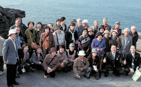 済州市龍譚洞（チェジュシ・ヨンダムドン）の龍頭（ヨンドゥ）岩を訪れた日本人団体観光客が２７日、記念撮影をしている。日本農協の優秀組合員で、約１０００人が３０日まで済州を観光する（済州コンベンションビューロー提供）。