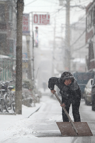 こちらのアジュンマ（おばさん）は、えっさえっさと道路の雪かき中。