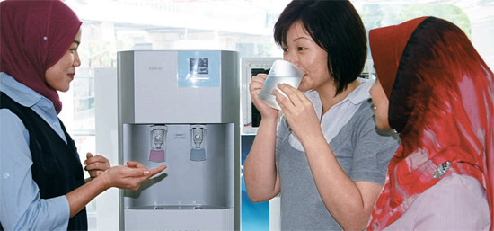 マレーシア・クアラルンプールの中心街にある熊津コーウェイの現地法人ショールームで顧客がコーディネーターの説明を聞きながら浄水器の水を味見している。