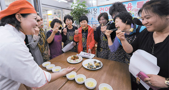 １２日、ソウル中区の新中部市場で乾物料理教室が開かれ、参加した商人と主婦が干し鱈を使った揚げ物や麺料理を試食している（写真＝ソウル中区庁）。