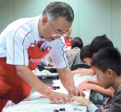 先月１３日、愛知県長久手市で開かれたトヨタの「科学のびっくり箱！」授業で、講師のサトウ・シゲアキさん（５９）が小学生にホバークラフト模型の製作方法を教えている。