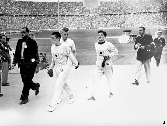 １９３６年８月９日、ベルリン五輪マラソン競技の表彰式場に向かう金メダリストの孫基禎と銅メダリストの南昇竜。胸に日章旗を付けている。写真の原本に説明はない。