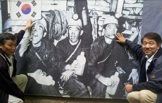 元鉱夫のファン・ソンボン館長（左）とキム・ヨンギル・ドイツ連邦政府家族省公務員が８月３１日、ドイツ・エッセン市の韓国人文化会館（ドイツ派遣鉱夫記念館）にある「鉱夫の昼食」の写真の前に座っている。