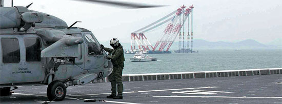 ２１日、クレーン船が見える事故海域に配置された独島艦で、米海軍ヘリコプターが離陸の準備をしている。韓米海軍は事故海域で共同救助作業を行っている。（写真＝米国防総省）