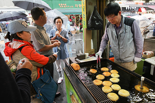 油で揚げた熱々のおやつ・ホットクの屋台には行列が。揚げたての香ばしい匂いに、道行く人も思わず足が止まってしまったのでしょうか。雨のなか食べるホットクもとてもおいしそう。