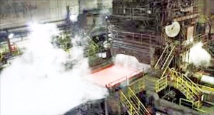 千葉県の新日鉄住金君津製鉄所内の熱延工場でスラブがローラーを通過しながら水蒸気を発している。（新日鉄住金提供）