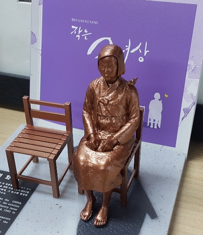 慰安婦少女像を製作した彫刻家のキム・ウンソン、キム・ソギョン夫妻がソウル中学洞（チュンハクトン）の日本大使館前の少女像に市民が着せた服と耳あてを直している。（写真＝中央フォト）