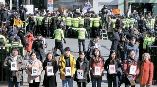 朴大統領弾劾審判最終弁論期日の２７日、憲法裁判所の前では弾劾賛否デモが続いた。環境運動連合の会員（前）がろうそく集会参加者から受けた弾劾要求葉書５８００枚を憲法裁民願室に伝えに行っている。同じ時間、憲法裁正門の向こうで保守性向の団体が弾劾反対デモを行った。