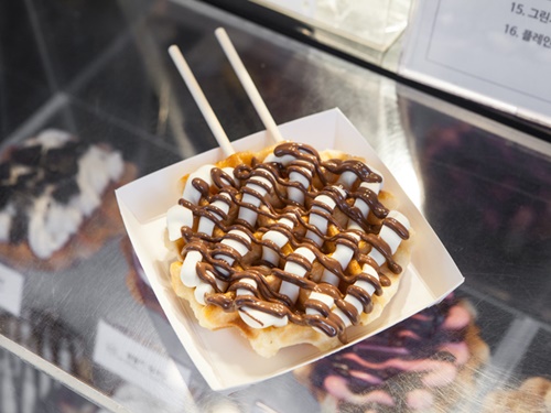 焼きたてのワッフルは歩きながら食べられるように、２本のスティックに刺してくれます（写真はヌテラクリームチーズ、３，０００ウォン）。冷めてもサクサクとしてまた違った美味しさがあるので、お持ち帰りでホテルで食べるのもあり。