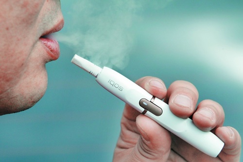 ある男性喫煙者が道路で電子たばこ製品「アイコス」を吸っている。（中央フォト）