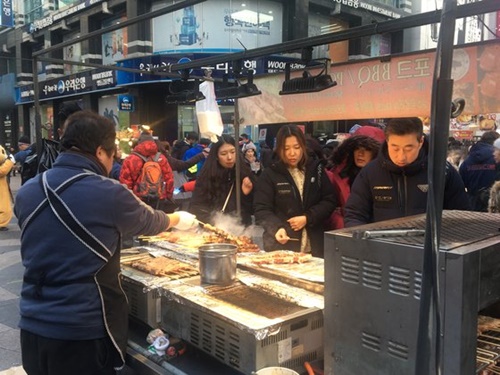 今月７日、ソウル中区明洞で中国人観光客がストリートフードの店でものを買って食べている。商人は「昨年の春節よりも観光客が減った」と話した。