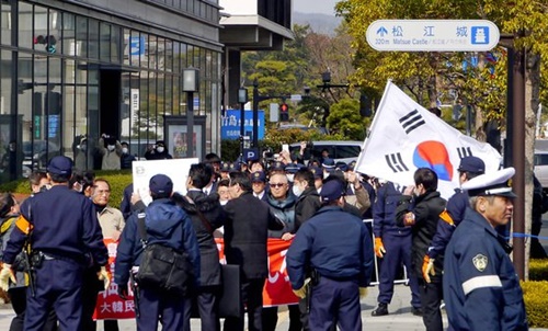 ２０１３年、島根県主催の「竹島の日」行事が開かれた県民会館の外で、独島守護全国連帯など韓国の市民団体会員が日本の警察に囲まれながら太極旗を持って抗議デモをしている（中央フォト）。