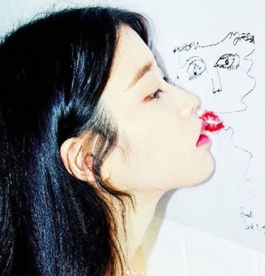 歌手のＩＵがソルリの自画像をバックにポーズを取っている。［写真　ＳＮＳ］