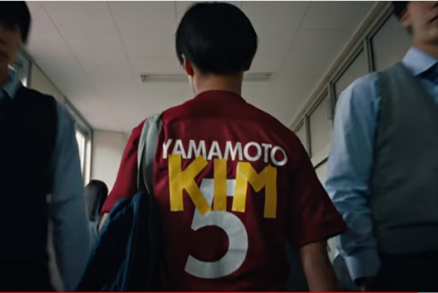 在日朝鮮人サッカー選手が日本式の名前「山本（ＹＡＭＡＭＯＴＯ）」の上に「キム（ＫＩＭ）」という名前を重ねたユニホームを着て歩いている。（写真ＹｏｕＴｕｂｅ画面キャプチャー）