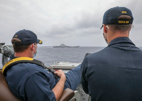 ４日にフィリピン海で米海軍のイージス艦マスティンで艦長（左）が艦橋の欄干に足を上げて中国海軍の空母遼寧を眺めている。［写真　米海軍］