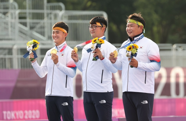 （左側から）キム・ジェドク、キム・ウジン、オ・セヒョク選手が２６日、東京夢の島公園アーチェリー場で開かれた東京オリンピック（五輪）男子アーチェリー団体メダル授与式で金メダルを手に笑顔を見せている。［写真　共同取材団］