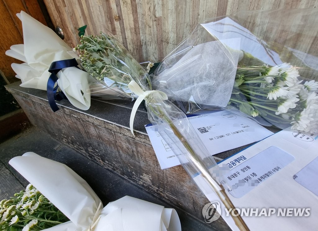 自殺した小商工人の店の前に置かれた菊の花と請求書。［写真　聯合ニュース］