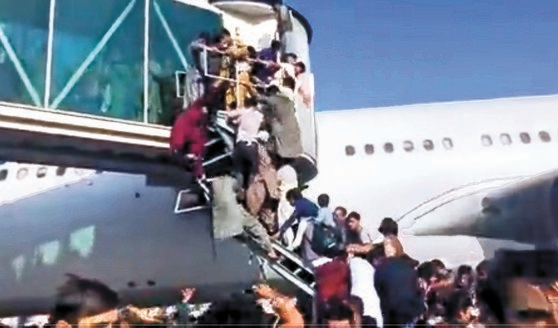 イスラム武装組織タリバンが政権を再掌握した昨年８月１６日、首都カブール空港からアフガニスタンを脱出しようとする人々が航空機に乗ろうと搭乗ブリッジにぶらさがり混乱を来している。［写真　ツイッター　キャプチャー］