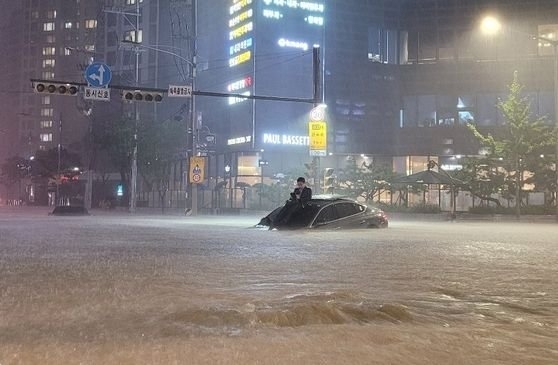 ８日、ソウルおよび京畿（キョンギ）北部地方に降った集中豪雨による被害写真がオンラインを通じて共有された。ある男性が浸水した車両の上に座って水難を避けている。［写真　オンライン掲示板　キャプチャー］