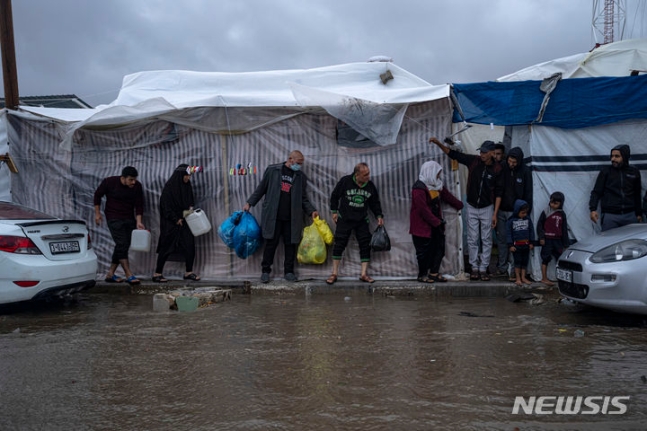 雨を避けて水の配給を受けるパレスチナ住民たち［写真　ＡＰ＝ニューシス］