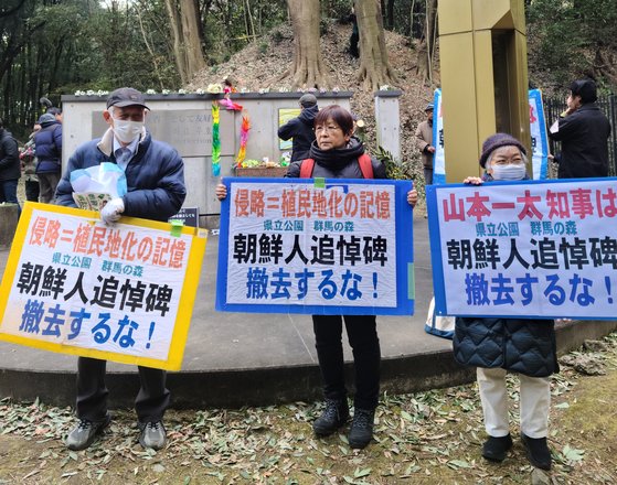 「追悼費　撤去するな」と書かれたプラカードを持っている日本市民。