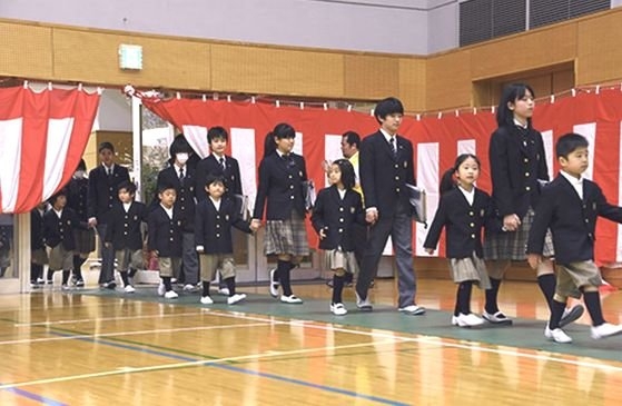 東京品川区にある日野学園の入学式。９年生の生徒が新入生の手を握って行事場所に入っている。小中学校を統合して９年制で運営しながら生まれた伝統だ。　［写真　品川区ホームページ］