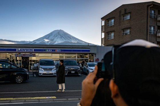 今年１月、ある観光客が富士山が見えるコンビニの前で写真を撮っている様子。［写真　ＡＦＰ＝聯合ニュース］