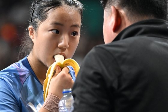 卓球女子シングルス８強戦の休憩時間に申裕斌（シン・ユビン）がバナナを食べながらオ・グァンホン監督の指示を聞いている。　キム・ソンリョン記者