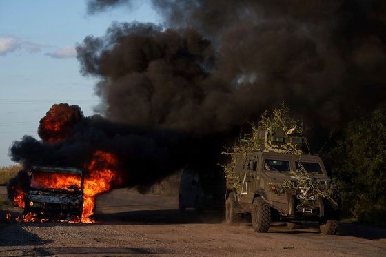 燃えている車を通り過ぎるウクライナ装甲車［写真　ＡＰ＝聯合ニュース］