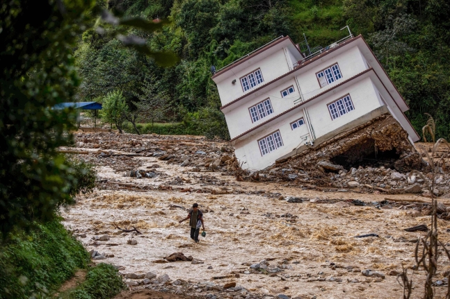 ネパールの洪水被害地域で濁流を横切る男性。［写真　ＡＦＰ＝聯合ニュース］