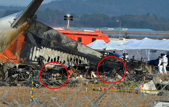 チェジュ航空機の乗客と乗務員１８１人中１７９人の死亡者が発生した務安国際空港の事故現場で３０日午後、警察と消防隊員が合同で現場鑑識を実施している。事故原因と指摘された旅客機のランディングギア（赤い円内）はひどく破損している。キム・ソンテ