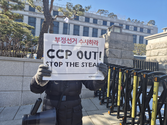 韓国憲法裁判所の前で「ＣＣＰ　ＯＵＴ」と書かれたプラカードを持っている集会参加者。チョン・ユル記者