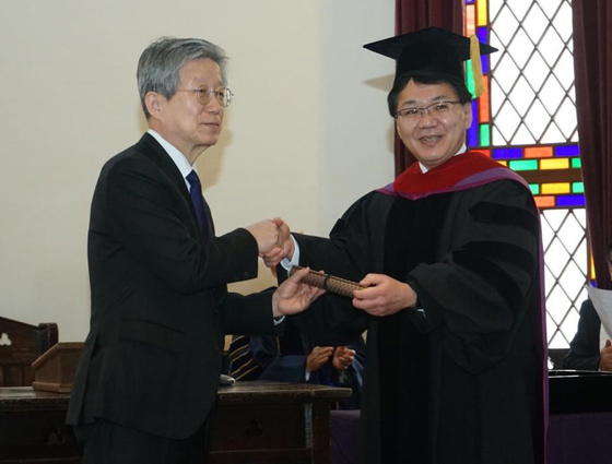 １６日、京都同志社大学で開かれた名誉博士学位授与式で尹東柱（ユン・ドンジュ）詩人の甥である成均館（ソンギュングァン）大学名誉教授のユン・インソク氏（左）と小原克博学長が握手をしている。［写真　在大阪韓国総領事館］