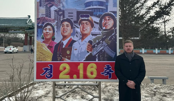 ジャスティン・マーテル氏が北朝鮮羅鮮市の宣伝看板前で残した記念写真。２月１６日は金正日総書記の誕生日だ。［インターネット　キャプチャー］