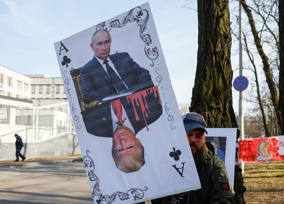 プーチン大統領とトランプ大統領の肖像画を持ってデモをする様子。［写真　ロイター＝聯合ニュース］