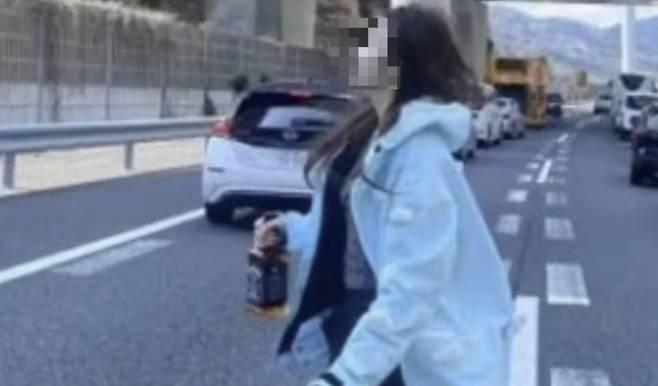 事故で渋滞した高速道路の真ん中でウイスキーのボトルを手にしている中国人女性。［写真　Ｘ］  ​