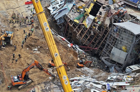 １６日、京畿道光明市一直洞の新安山線複線電鉄５－２工区崩壊現場で、消防士など関係者が行方不明者の捜索作業を行っている。［写真　ニュース１］