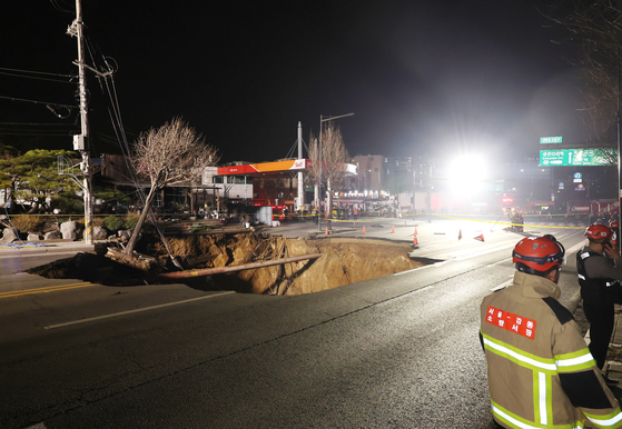 先月２４日、シンクホール（道路陥没）事故が発生したソウル江東区明逸洞（カンドング・ミョンイルトン）デミョン小学校付近の交差点で消防隊員が現場捜索および救助作業を準備している。　［聯合ニュース］