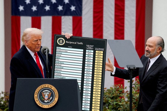 米国のドナルド・トランプ大統領（左）が４月２日、ワシントンＤ．Ｃ．ホワイトハウスのローズガーデンで各交易対象国に対する相互関税を発表している。トランプ氏が発言する間、ハワード・ラトニック商務長官が相互関税関連のチャートを支えている。［写真　ロイター＝聯合ニュース］