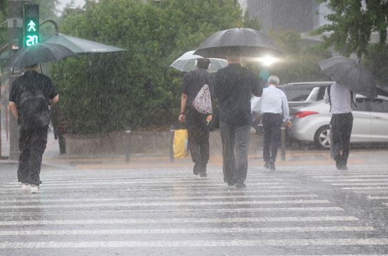 ソウル西南部に大雨注意報が発令された８日、ソウル永登浦区汝矣島（ヨンドゥンポグ・ヨイド）の国会近くで、市民たちが傘をさして横断歩道を渡っている。［写真　聯合ニュース］