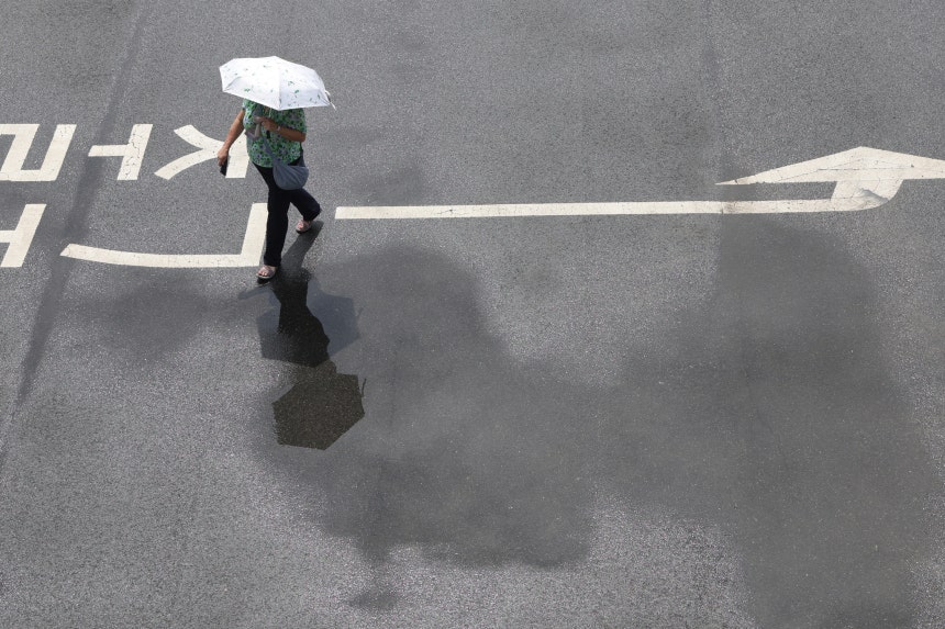 日傘を差した歩行者が梅雨の雨で濡れた地面を歩いている。［写真　聯合ニュース］