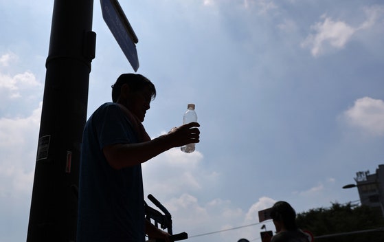 猛暑が続く中、２８日ソウル東大門（トンデムン）総合市場付近で、作業員が布地を運んだ後に水を飲んで休息を取っている。［写真　聯合ニュース］