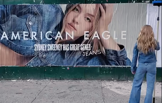 ハリウッド女優シドニー・スウィーニーが出演した米国のアパレルブランド「アメリカンイーグル」のジーンズ広告の一場面。壁に書かれた「Ｇｅｎｅｓ」という文字をめぐって、米国の進歩（リベラル）陣営からは優生学への懸念が出ているが、保守派は「過剰な解釈」だと反論している。［アメリカンイーグル公式ＹｏｕＴｕｂｅ　キャプチャー］