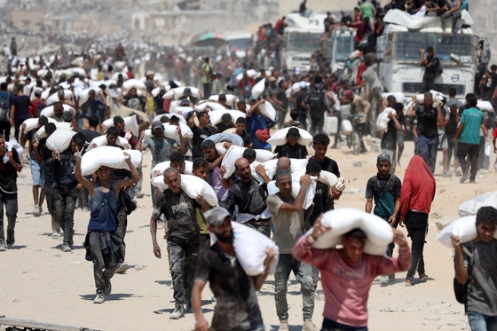 ７月２７日（現地時間）、ガザ地区北部のベイト・ラヒアで、パレスチナ住民たちが救援物資の小麦粉の袋を運んでいる。イスラエルは人道支援を保障するため、当面の間、毎日午前１０時から１０時間、ガザ地区の人口密集地域３カ所で軍事作戦を中断することにした。［写真　新華社通信＝聯合ニュース］