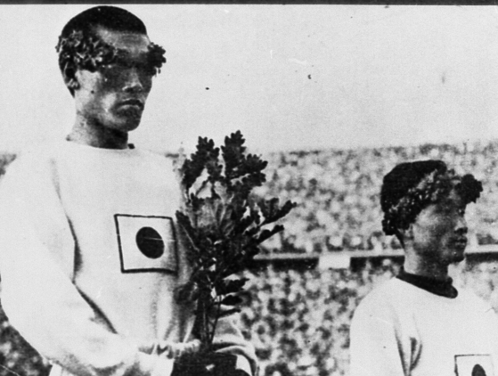 １９３６年ベルリンオリンピック（五輪）のマラソンで優勝後、表彰台に上がる孫基禎（ソン・ギジョン）選手。月桂樹の若木を、胸につけられた日章旗のところまで引き寄せて抱えている。［中央フォト］