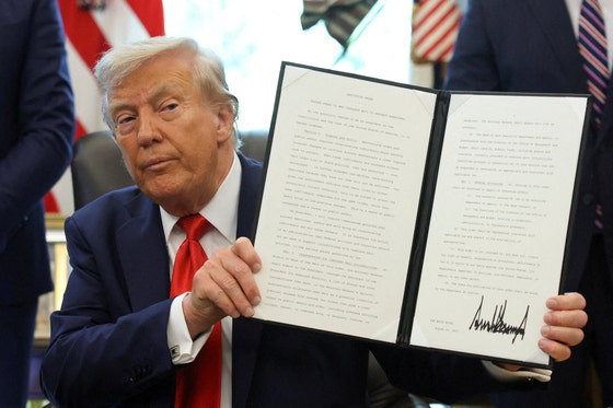ドナルド・トランプ米大統領が２５日（現地時間）、米ワシントンＤＣのホワイトハウス執務室で行政命令に署名した後、持ち上げている。［写真　ロイター＝聯合ニュース］