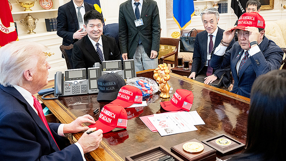  トランプ大統領と会い「MAGA」の帽子をかぶる日本の経済財生担当相。［写真 ロイター＝聯合ニュース］