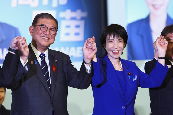 自民党の新総裁に選出された高市氏が石破氏と手を取り合う様子。［EPA＝聯合ニュース］